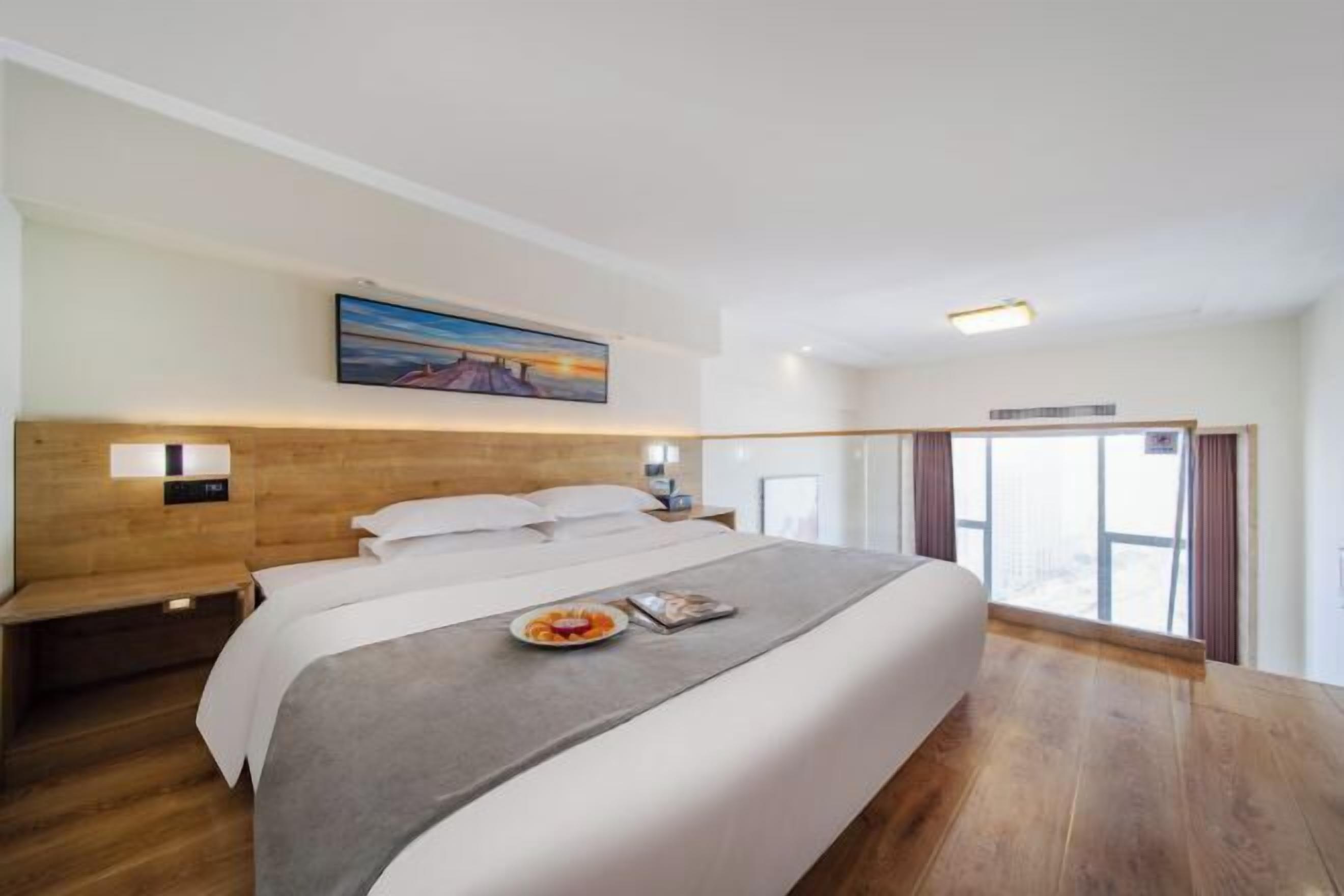 Een moderne hotelkamer met een groot bed, een houten hoofdbord, nachtkastjes en uitzicht door een glazen deur.