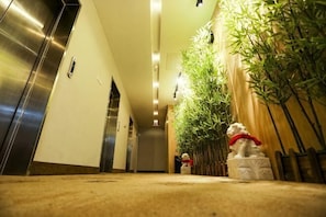 A hotel hallway with an elevator, a reception desk, and a decorative plant. - Timeless Hotel (Yantai)