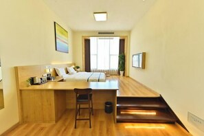 A compact hotel room with a bed, a small desk with a chair, a window with curtains, and a staircase. - Timeless Hotel (Yantai)
