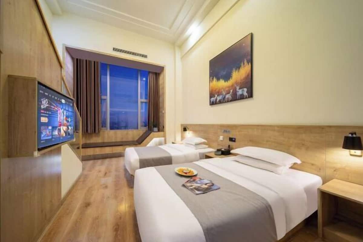 A hotel room with two beds, a TV, a painting, and a window with curtains.