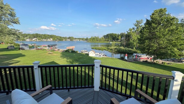 A deck with outdoor seating and a view of a lake with boats and houses in the background. - Lakefront Getaway on Murray Lake - Swim, Fish, Float, & Relax (Lowell)
