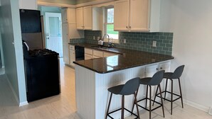 A modern kitchen with white cabinetry, a granite countertop, and a built-in island with bar stools. - Lakefront Getaway on Murray Lake - Swim, Fish, Float, & Relax (Lowell)