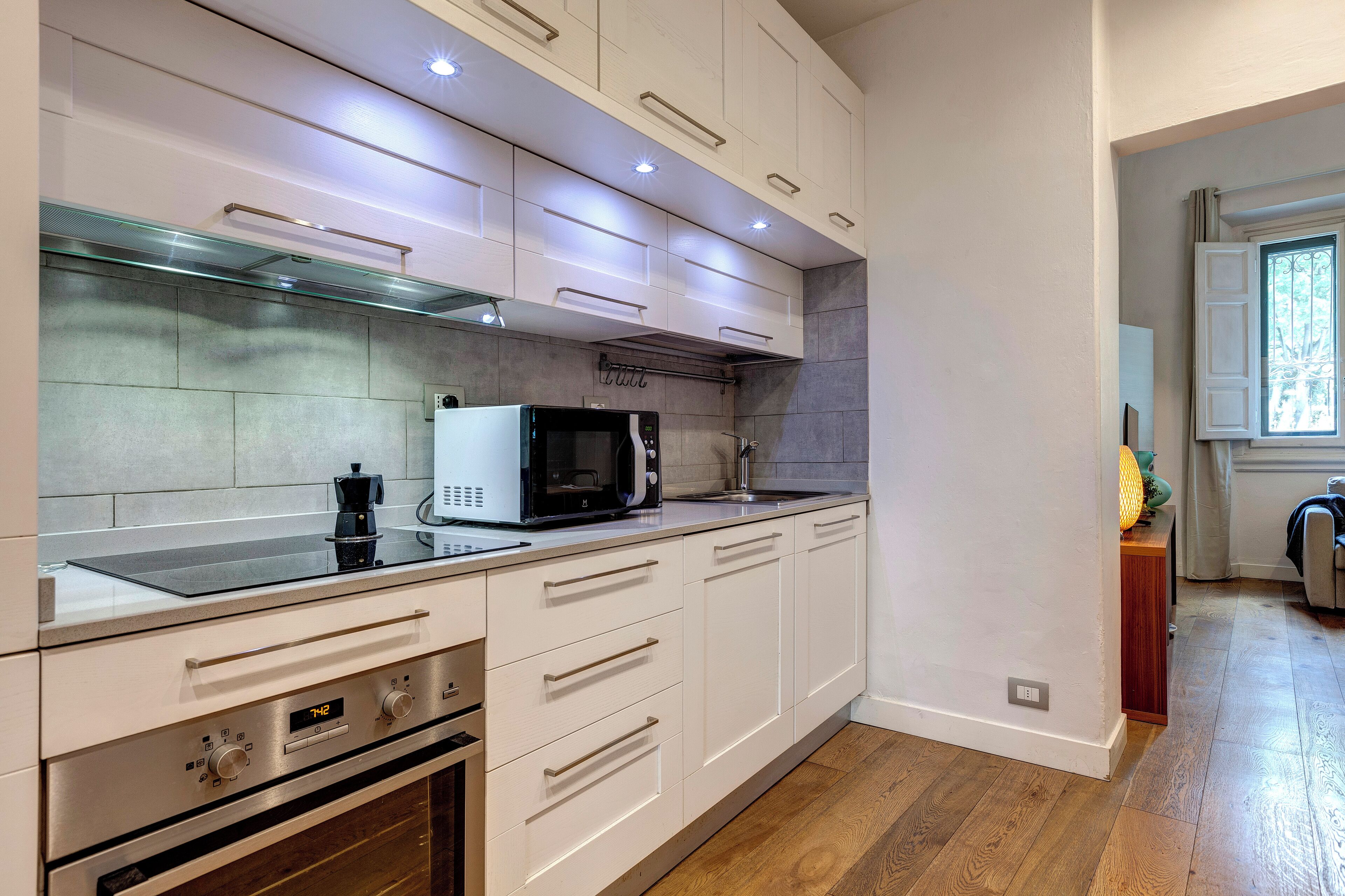 Una cocina moderna con armarios blancos, electrodomésticos de acero inoxidable y suelo de madera.