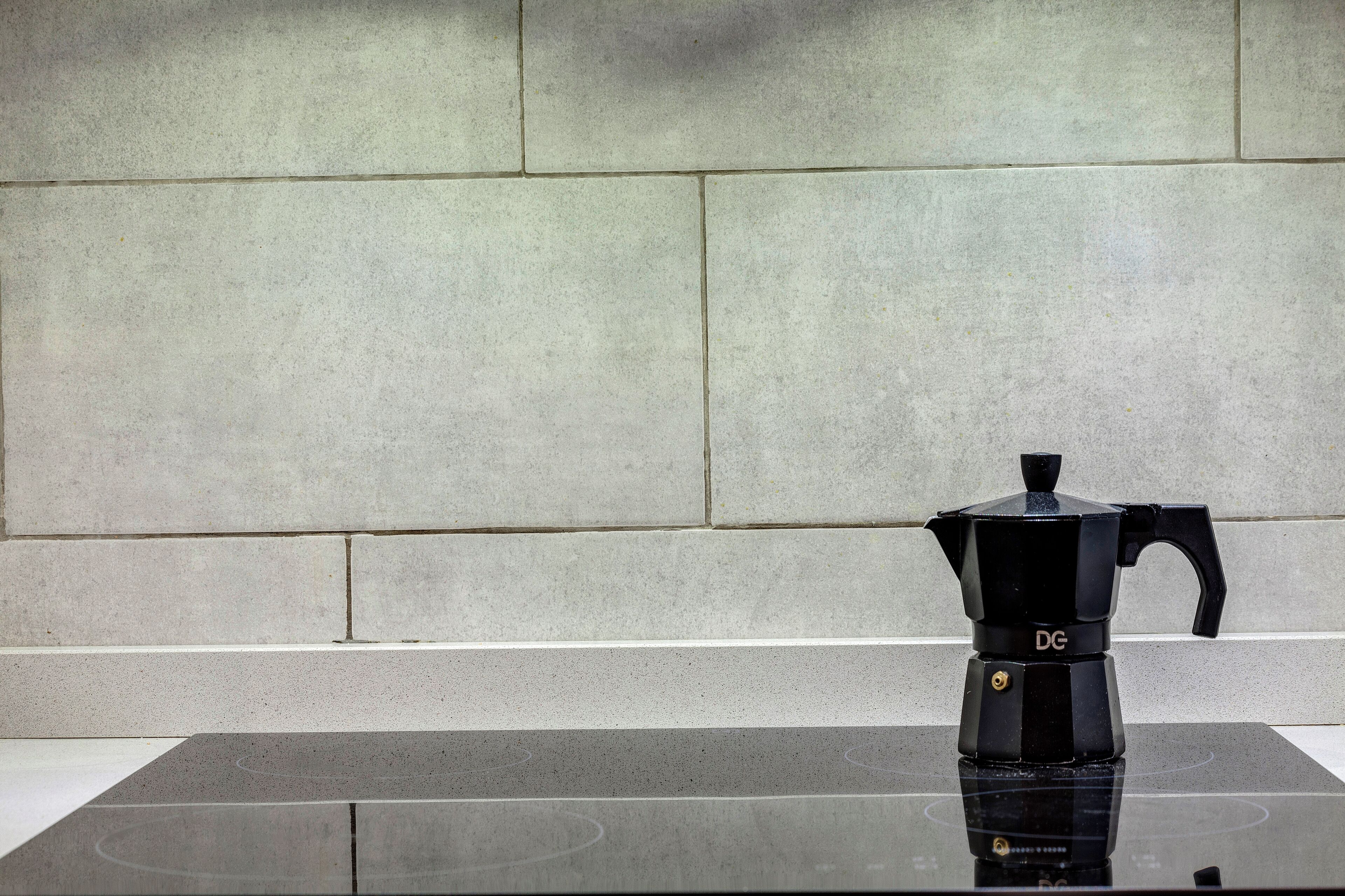 A black coffee maker on a reflective black surface against a tiled wall.