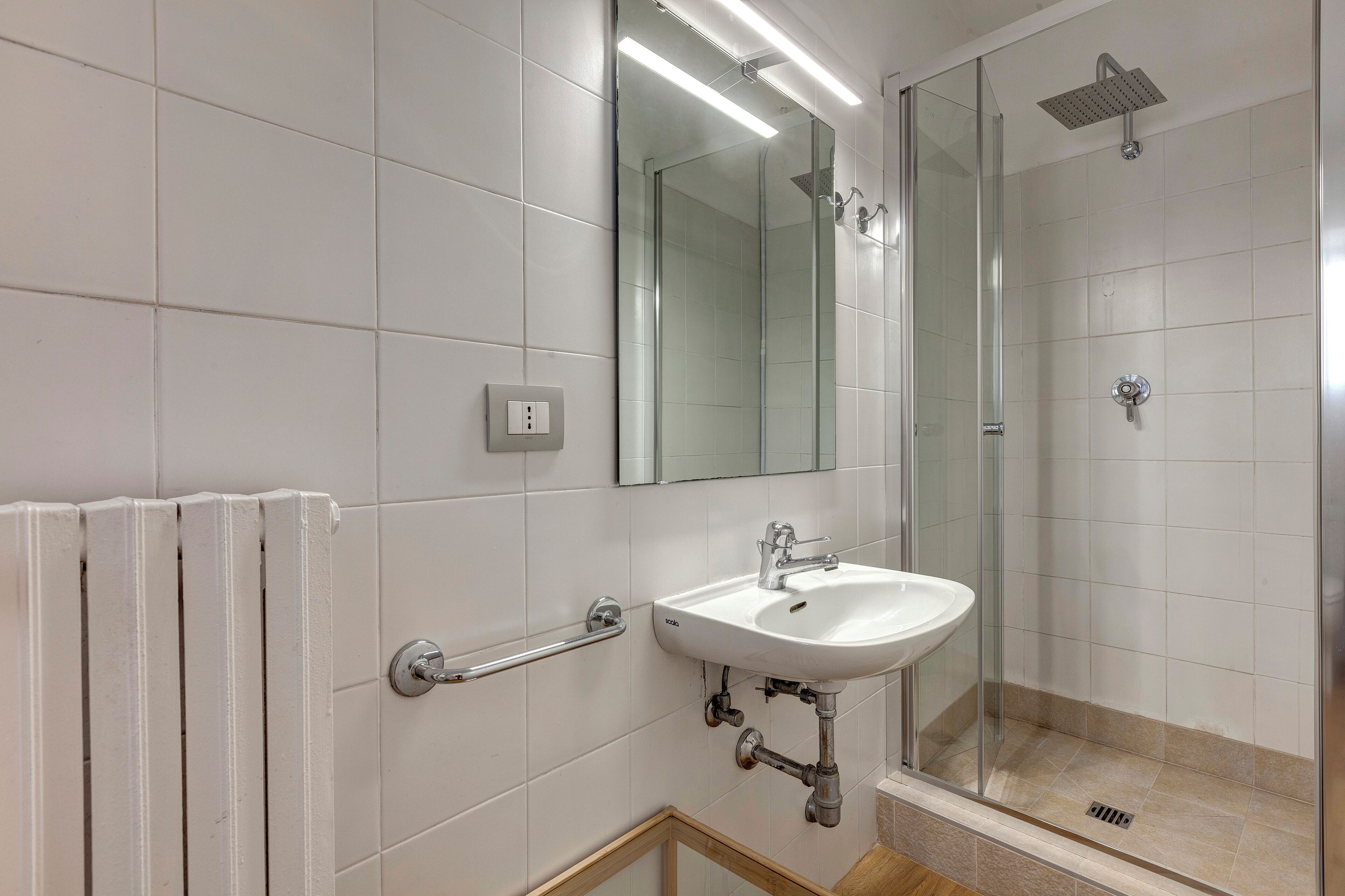 Une salle de bain moderne avec une douche à parois de verre, un lavabo blanc et une barre d’appui.