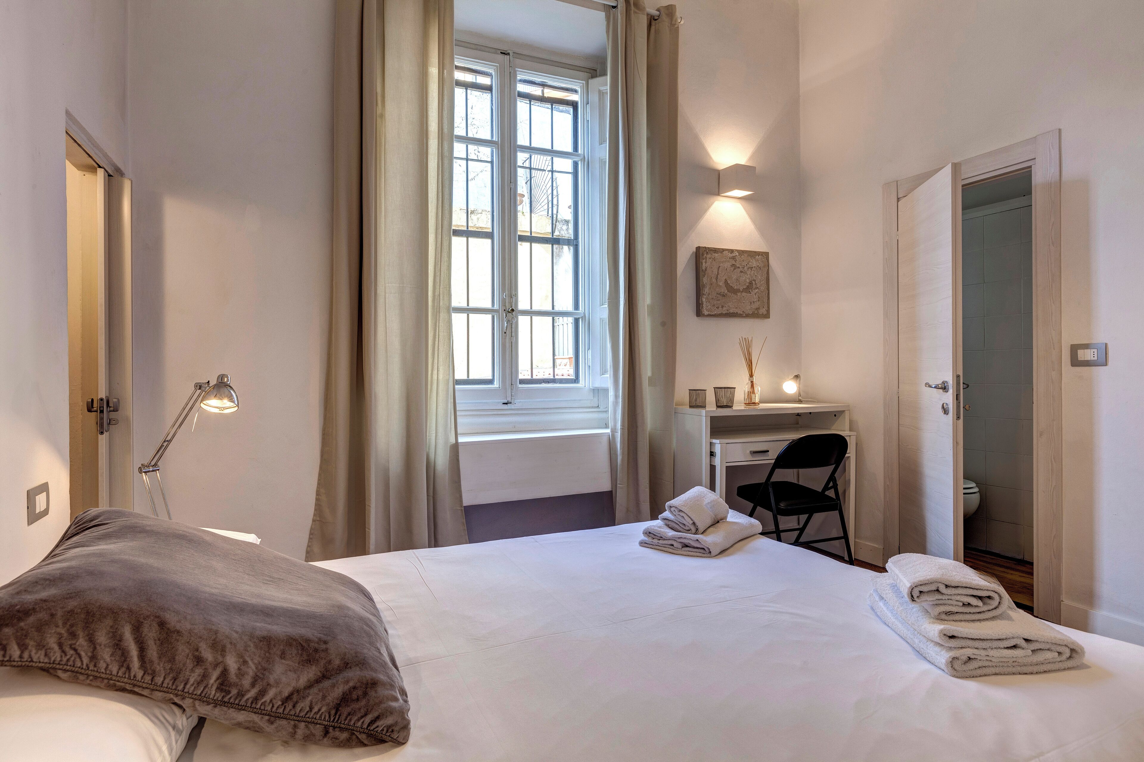 A hotel room with a bed, a desk, a chair, and a bathroom visible through an open door.