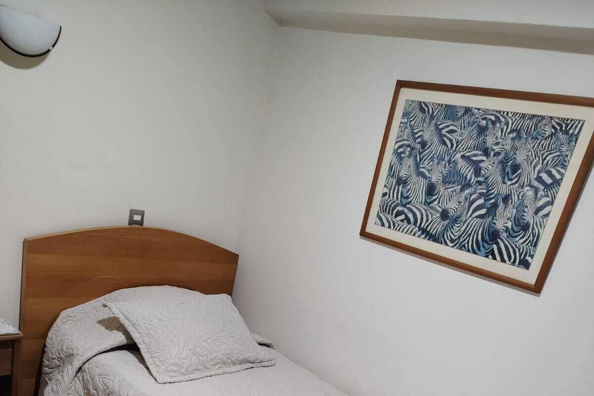 A single bed with a wooden headboard, a white quilt, and a framed zebra print on the wall.