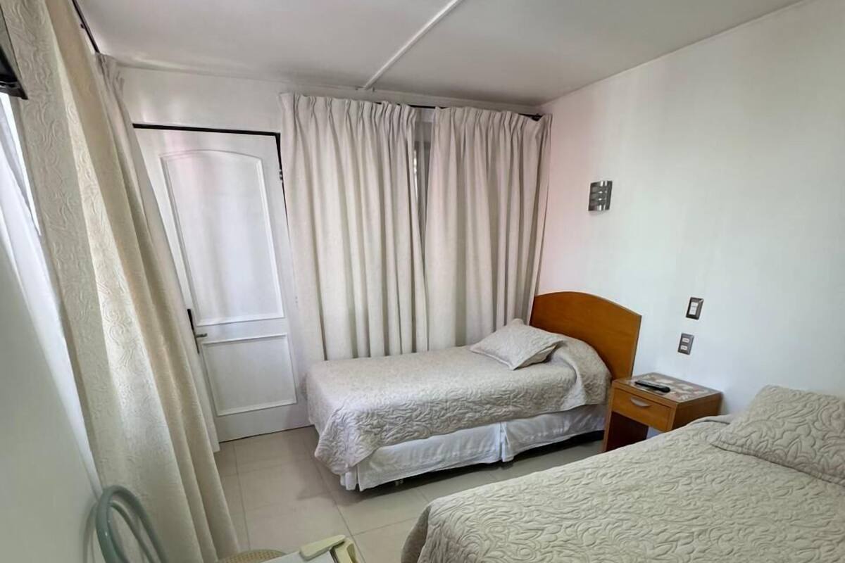 A hotel room with two beds, a desk with glasses, a nightstand, and a ceiling light.