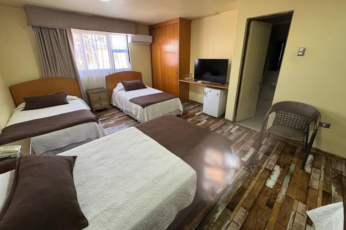 A hotel room with three beds, a television, a small desk, and a chair.