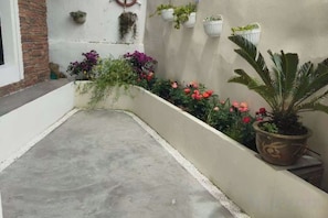 Une terrasse en béton avec un mur blanc, des plantes en pot et un mur de briques sur la gauche.