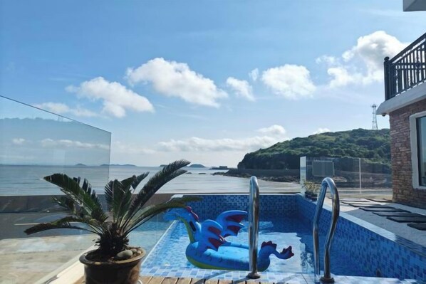 Une piscine aux motifs bleus et blancs, une plante en pot et une vue sur la mer et les collines.