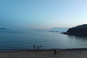 Une plage avec une eau calme, des reliefs lointains et quelques personnes.
