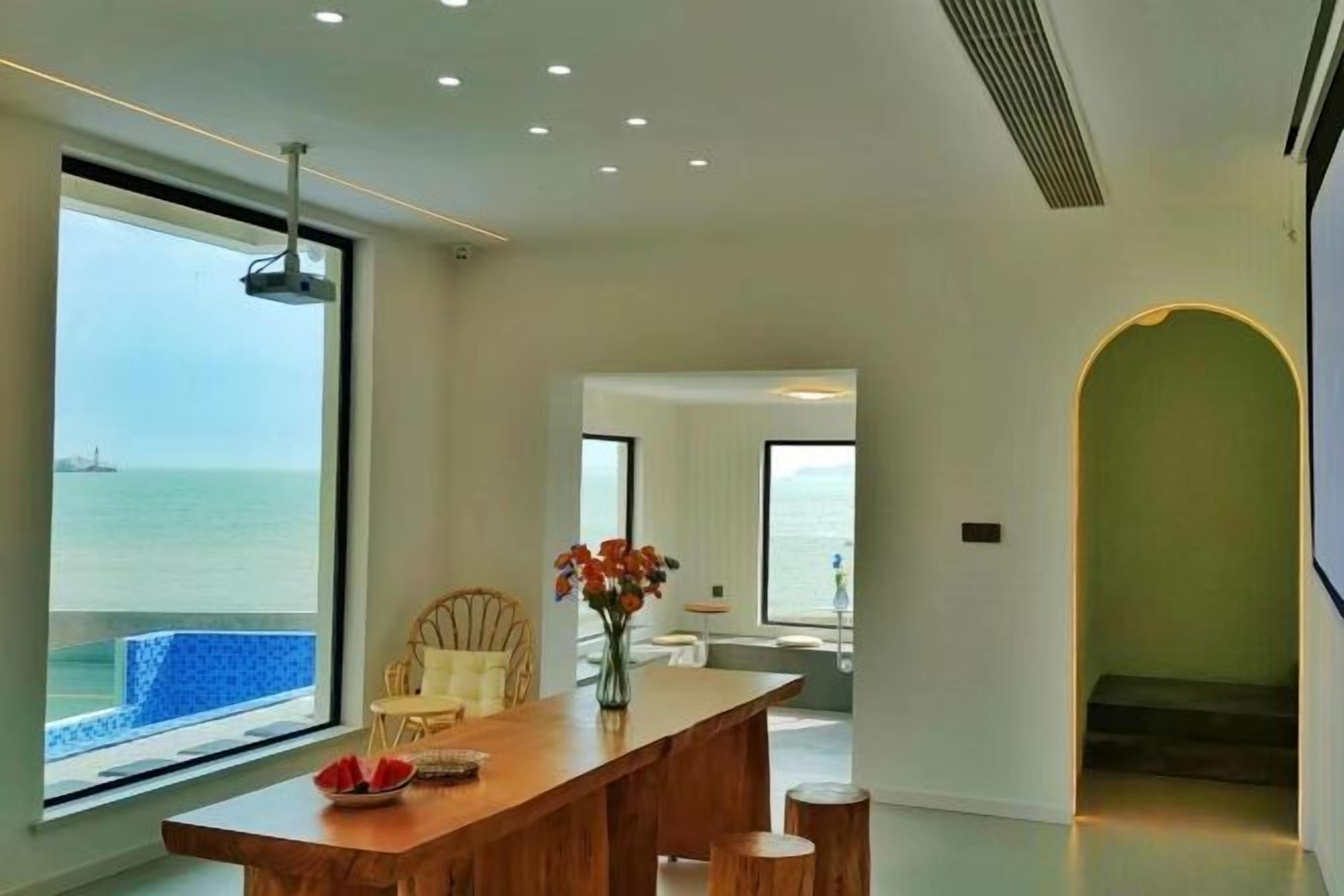A modern interior with a large window overlooking the sea, a wooden dining table, and a staircase leading to another level.