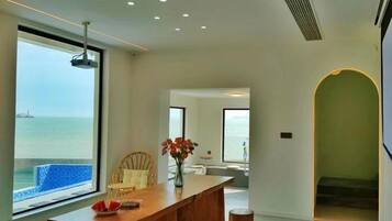 A modern interior with a large window overlooking the sea, a wooden dining table, and a staircase leading to another level.