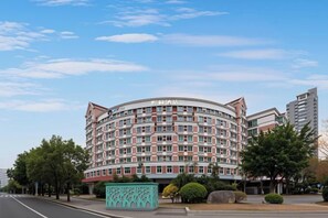 A multi-story hotel with a curved facade, a central entrance, and a parking area with trees. - Yuelin Hotel (Fuzhou)
