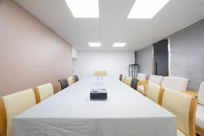 Une salle de conférence avec une longue table, des chaises, un projecteur et une fenêtre.