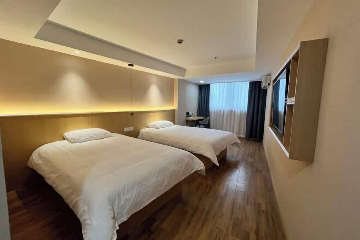 A hotel room with two beds, a desk, and a large window with curtains.