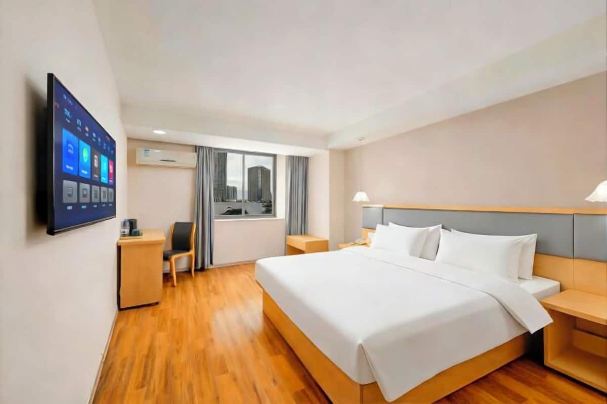 A hotel room with a large bed, a desk, a chair, a TV, and a window with curtains.