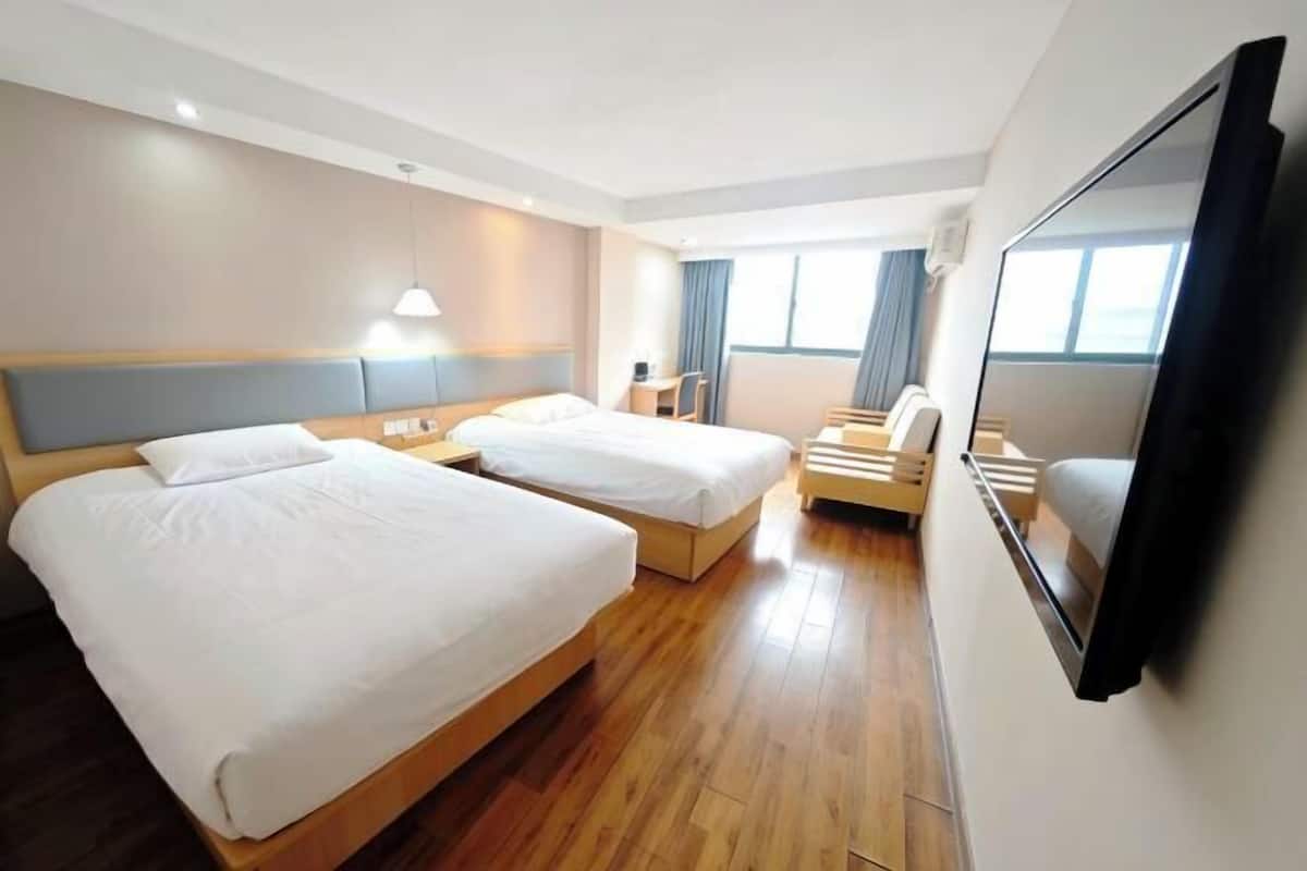 A hotel room with two beds, a desk, a chair, a TV, and a large window.