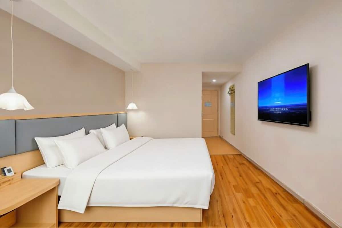 A modern hotel room with a large bed, bedside tables, a flat-screen TV, and a view of the cityscape.