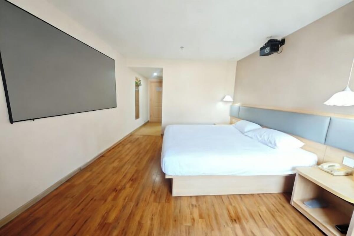 A modern hotel room with a large bed, a bedside table with a lamp, and a flat-screen TV mounted on the wall.
