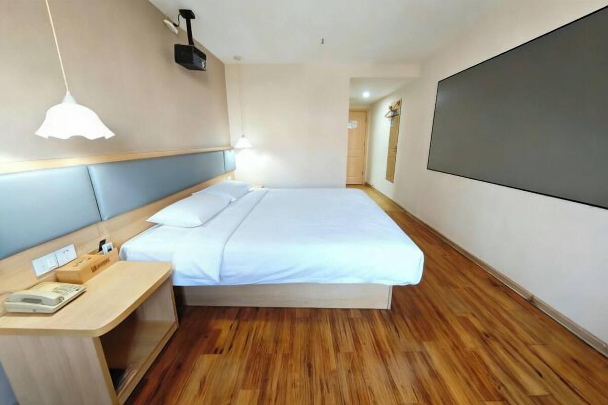 A hotel room with a bed, bedside table, and a large TV screen.