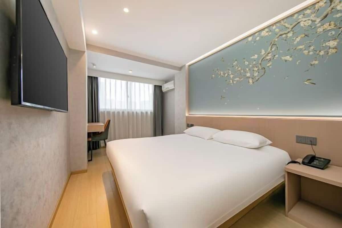 A hotel room with a bed, a desk, a chair, a TV, and a wall with a floral design.