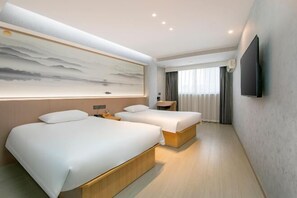 Una habitación de hotel moderna con dos camas, un televisor grande montado en la pared y un cuadro sobre las camas.
