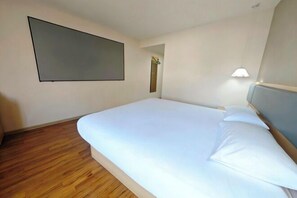 A hotel room with a large bed, a flat-screen TV mounted on the wall, a bedside lamp, and a wooden floor.