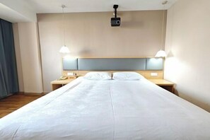 A hotel room with a large bed, two bedside tables, a projector mounted on the ceiling, and two pendant lights.