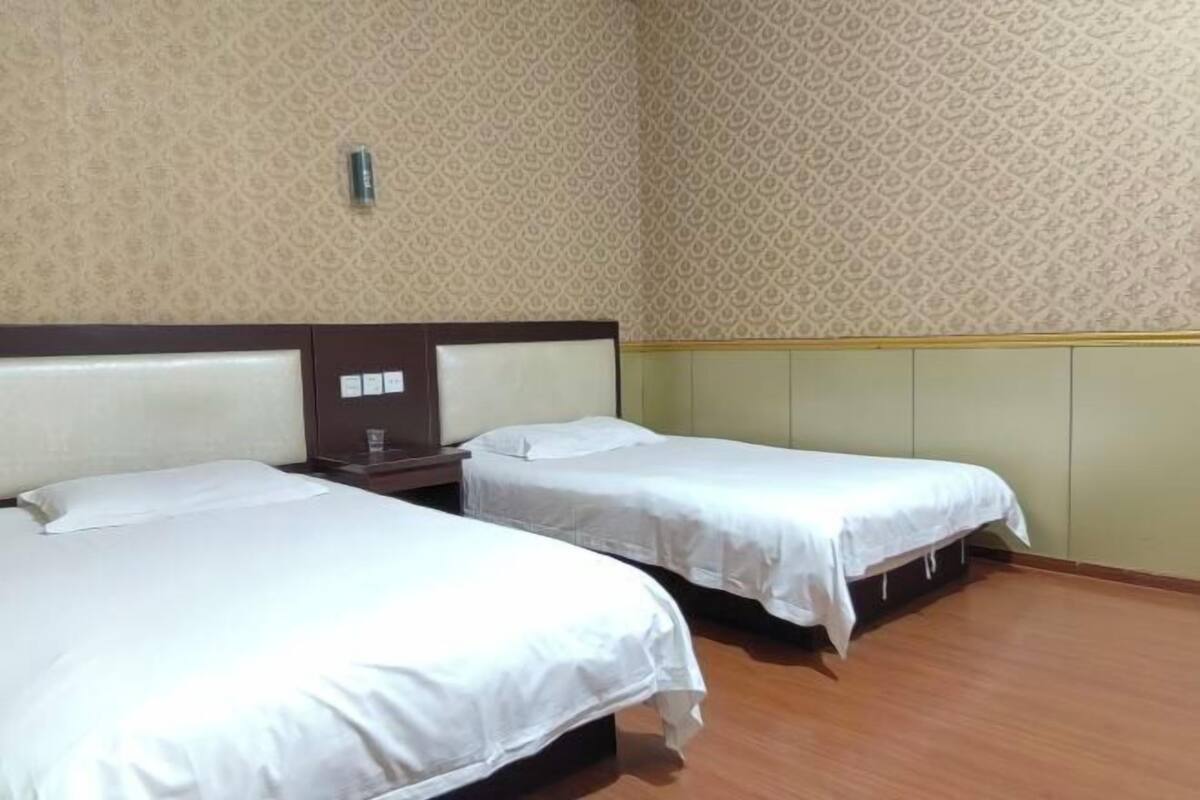 A hotel room with two beds, a wooden headboard, a patterned wallpaper, and a light-colored floor.