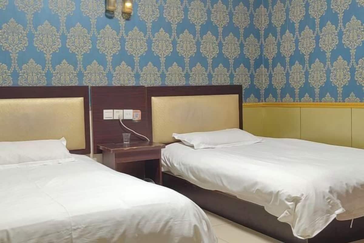 A hotel room with two single beds, a wooden nightstand, and a wall-mounted light fixture.