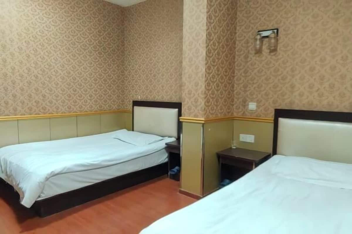 A hotel room with two beds, a small table, and a wall-mounted light fixture.