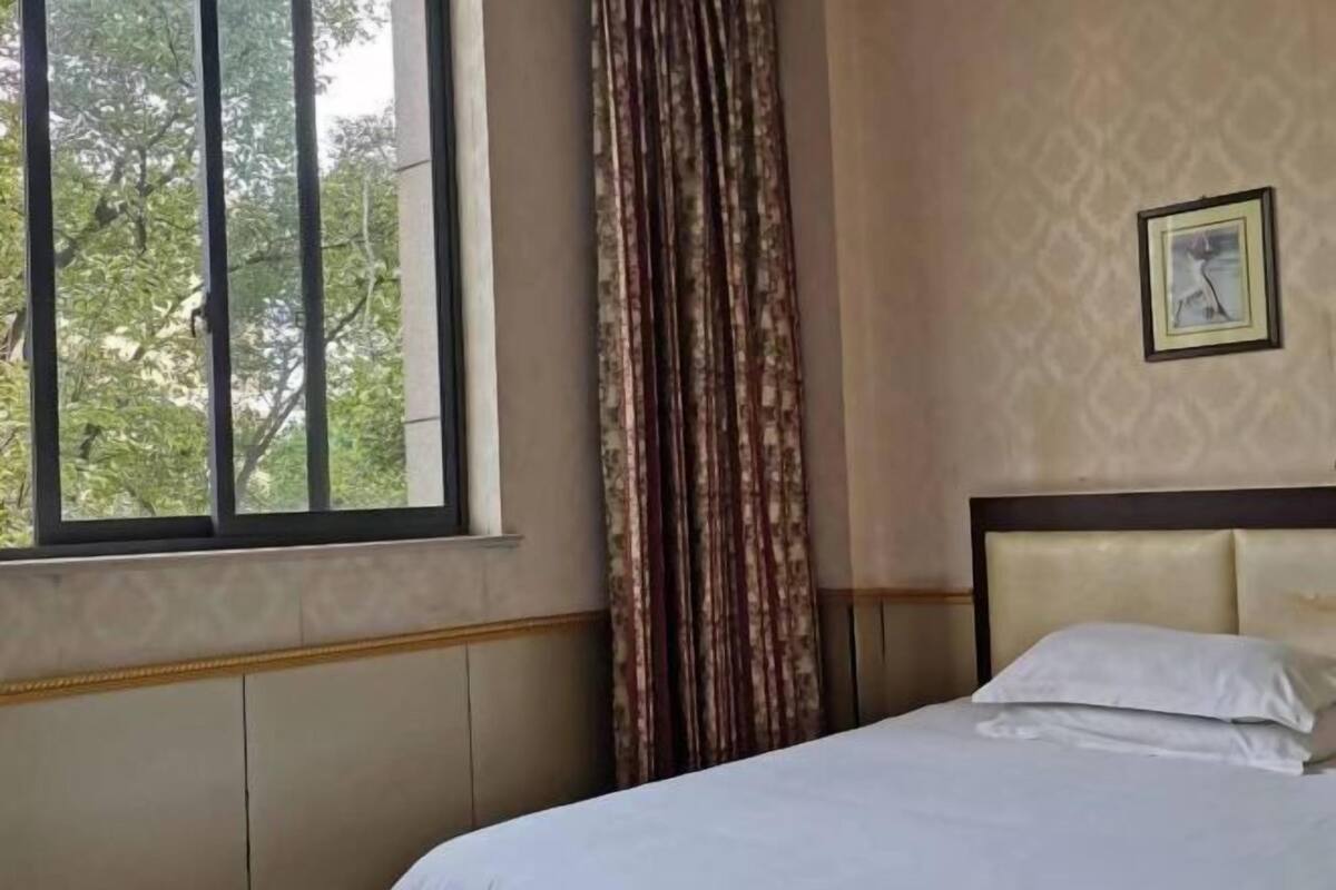 A hotel room with a bed, a window with blinds, a curtain, and a framed picture on the wall.