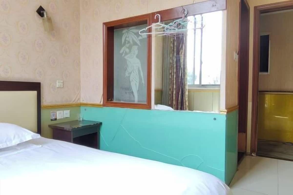 A hotel room with a bed, a small table, a mirror with a window, and a door.