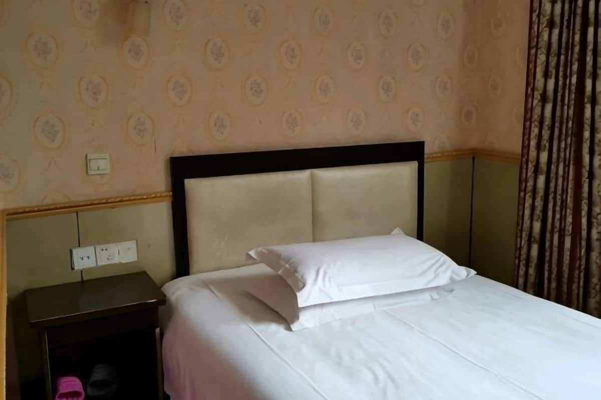 A hotel room with a bed, a nightstand, and a power outlet on the wall.