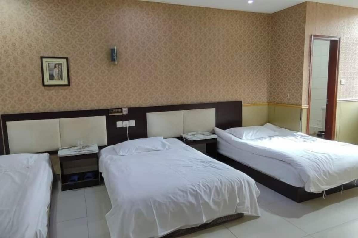 A hotel room with three beds, a headboard, a bedside table, and a wall-mounted light fixture.