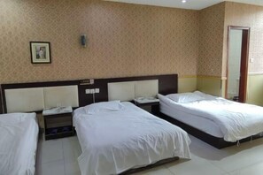 Une chambre d’hôtel avec trois lits, une tête de lit, une table de chevet et un luminaire fixé au mur.