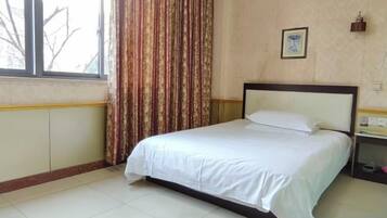 Uma cama de solteiro com colchão e cabeceira brancos em um quarto com janela e cortinas.