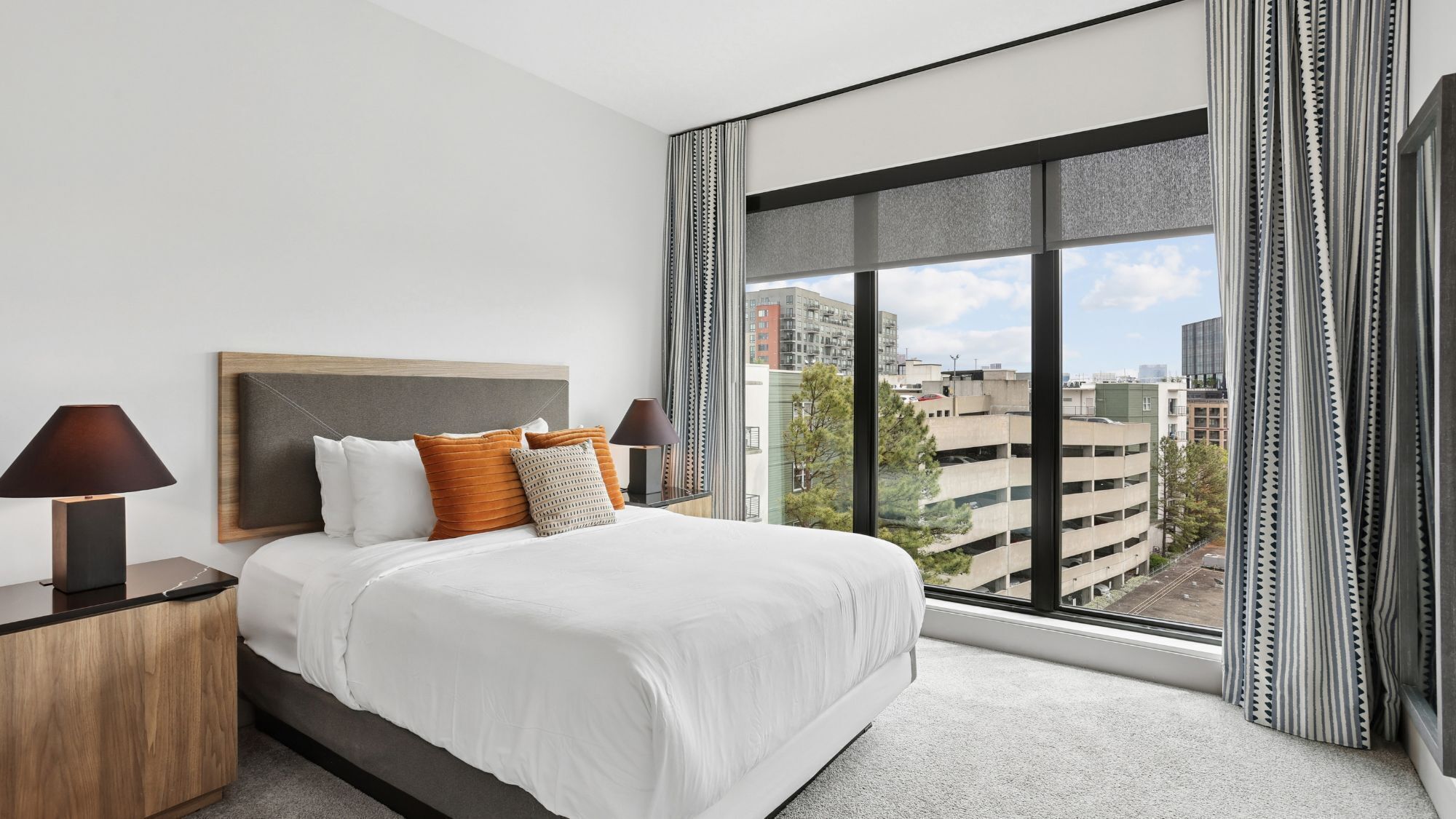 A hotel room with a large bed, two bedside tables, a view of the city through a large window, and a cityscape visible outside.