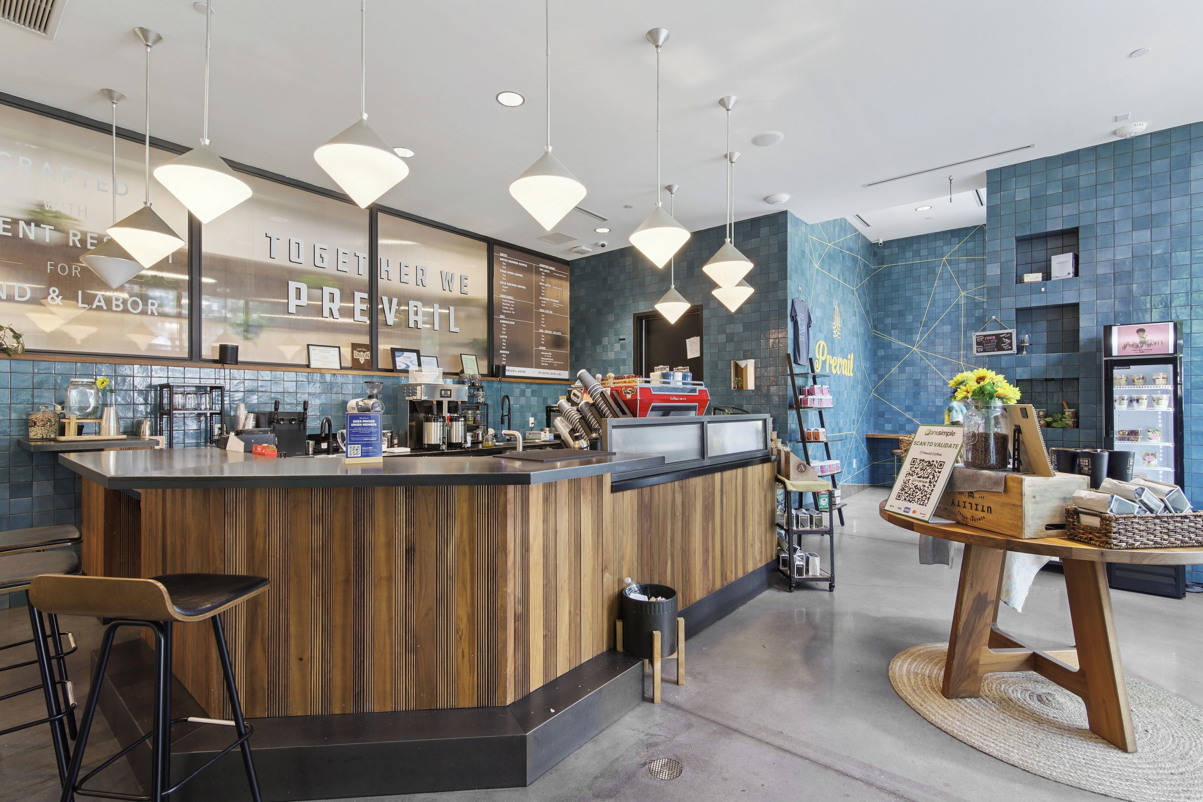 Un espace bar moderne avec un comptoir en bois, des luminaires suspendus et un mur recouvert de carreaux bleus.
