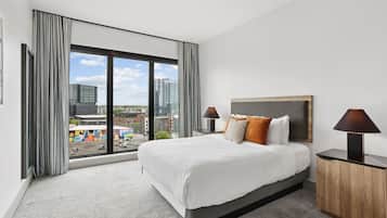 A modern hotel room with a large bed, two bedside lamps, a view of the cityscape, and a large window with curtains.