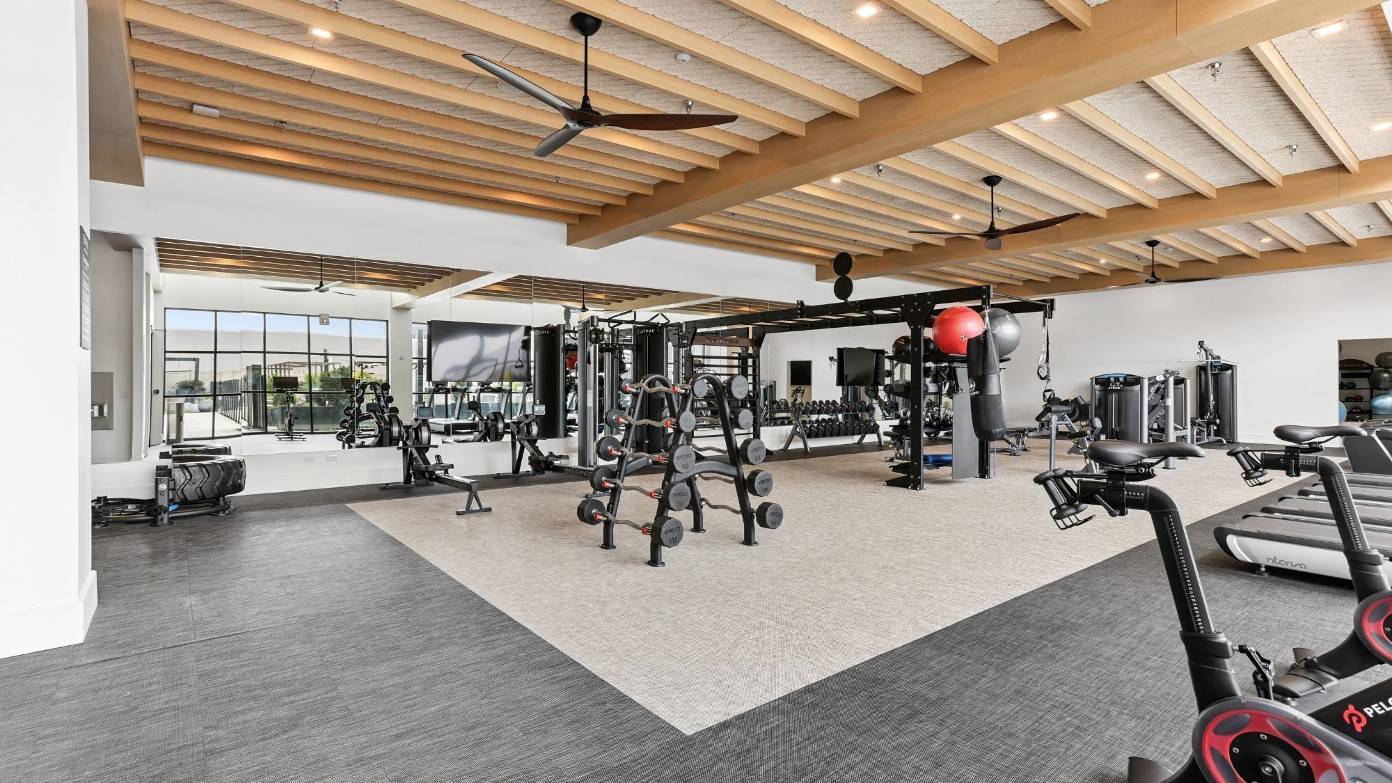 A gym with various exercise equipment, large windows, and a ceiling with wooden beams.