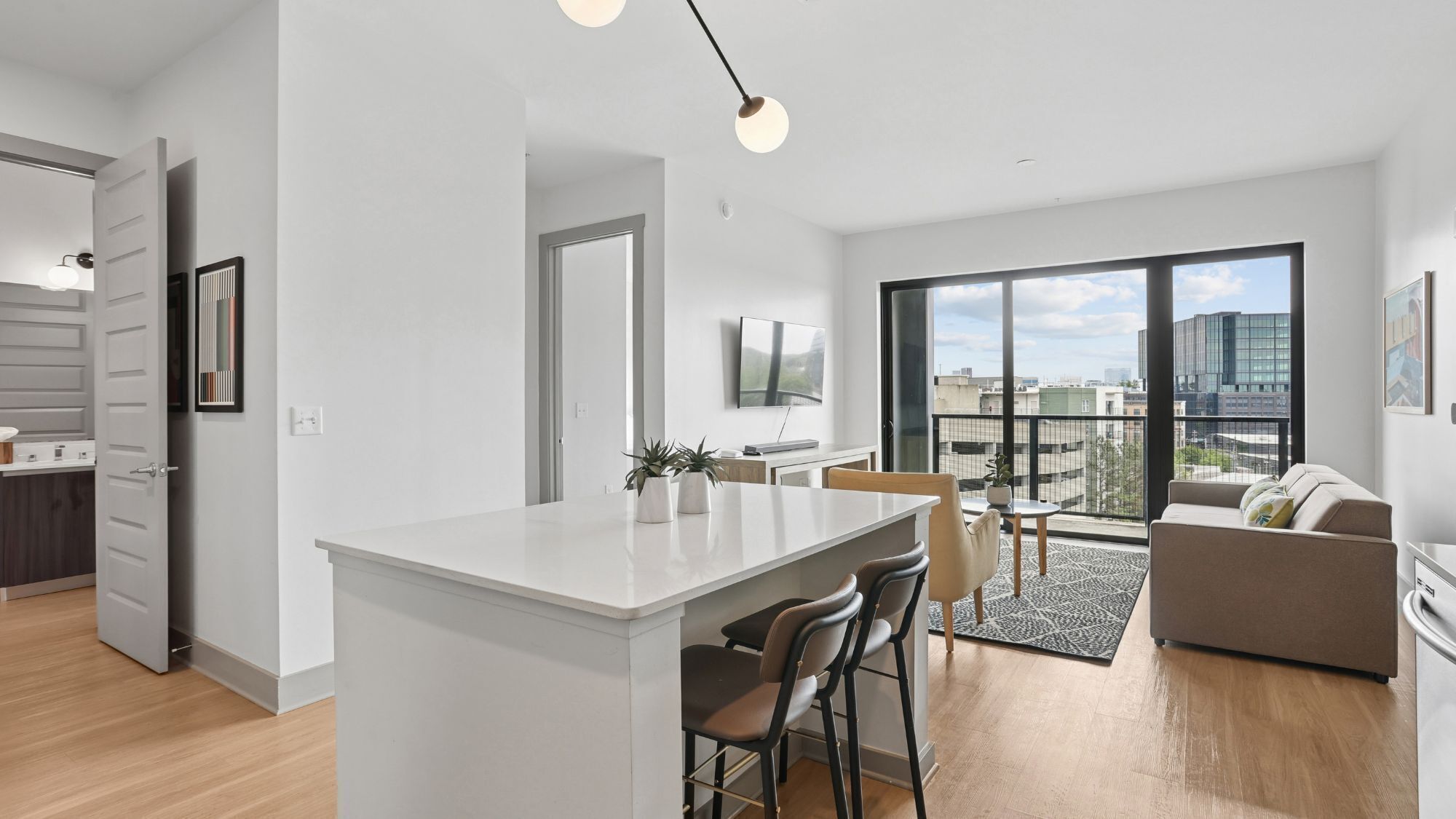 A modern apartment with a kitchen, dining area, and a balcony with a city view.