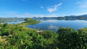 A serene lake surrounded by lush greenery and distant mountains under a clear blue sky. - Ineza Guest House (Kinoni)