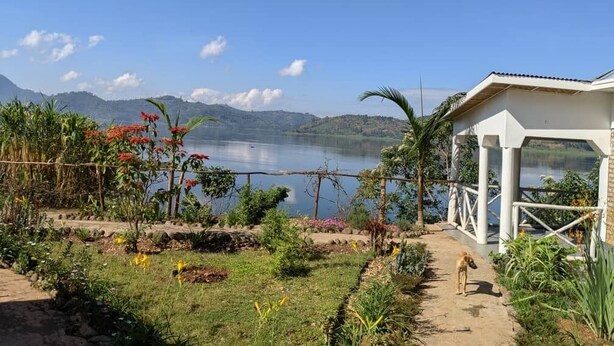 A garden with a pathway leading to a white gazebo overlooking a lake with mountains in the background. - Ineza Guest House (Kinoni)