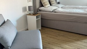 Et moderne soveværelse med en grå sofa, en seng med hvidt sengetøj, et natbord med en lampe og dekorative elementer på væggen.