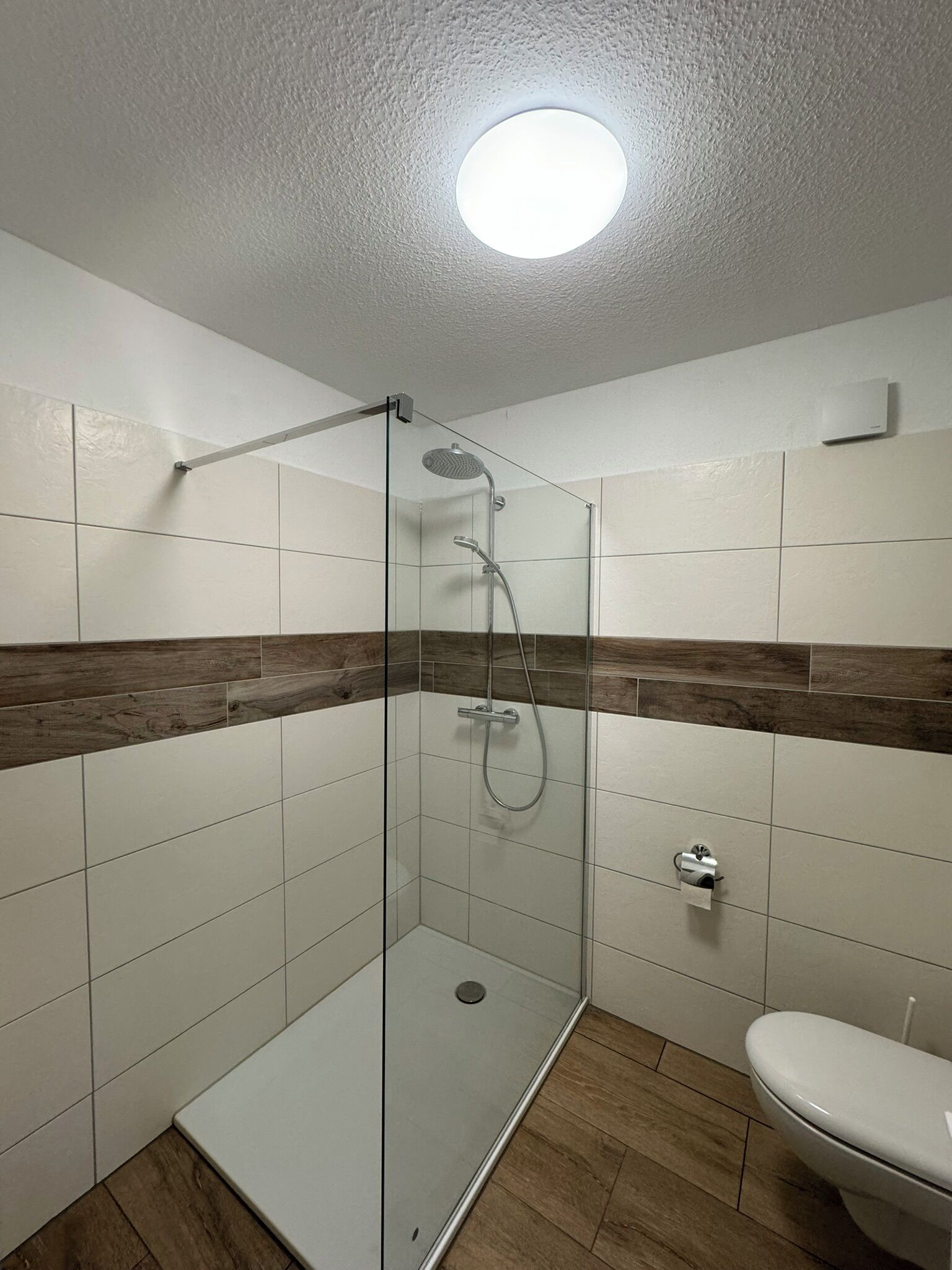 A modern bathroom with a glass shower enclosure, white tiles, wooden accents, and a toilet.