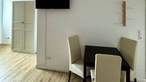En moderne stue med et fladskærms-tv på væggen, et spisebord med stole, et garderobeskab og en loftlampe.