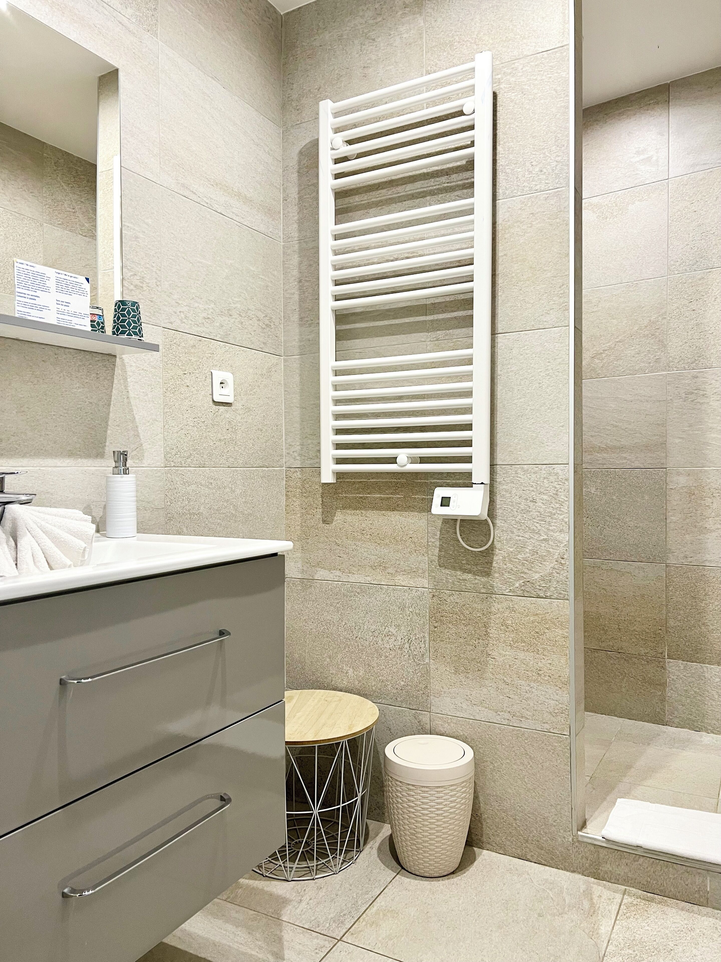 Un baño moderno con un toallero blanco, un cesto de basura redondo y un espejo pequeño y circular.